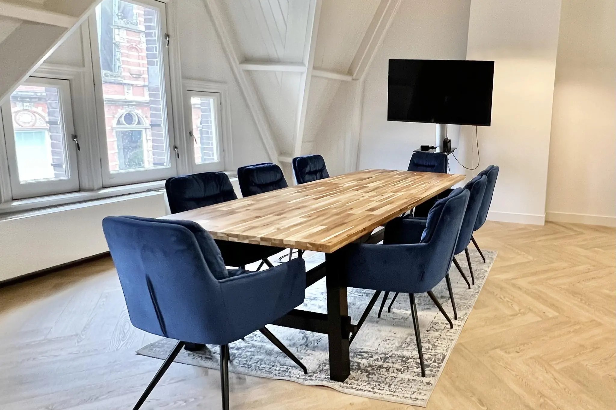 Vergaderruimte met houten tafel, acht blauwe stoelen en flatscreen-tv aan de Paulus Potterstraat.