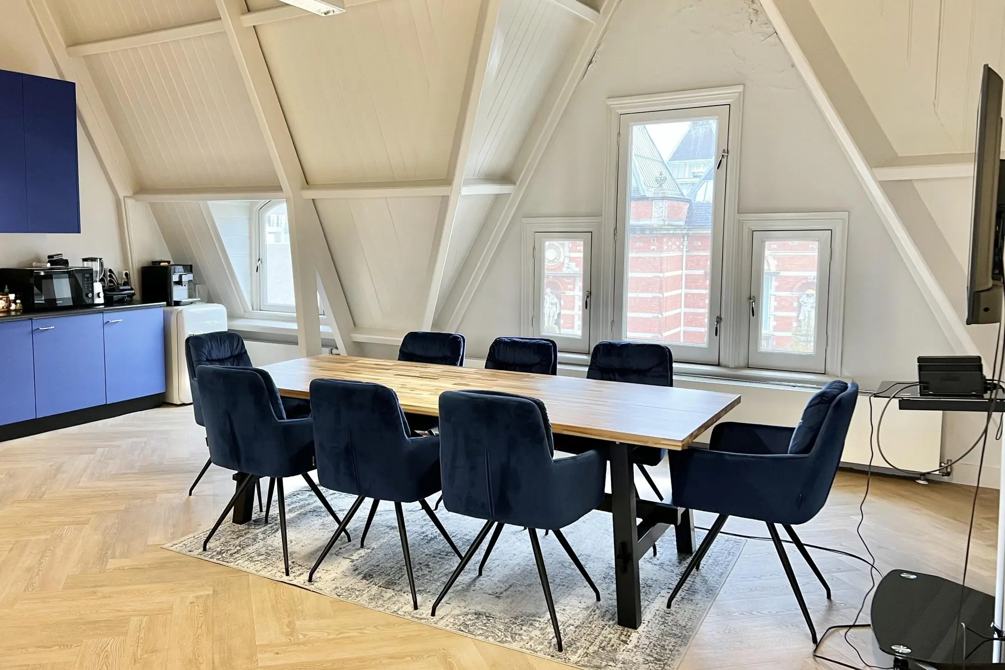 Vergaderruimte aan de Paulus Potterstraat met houten tafel, blauwe stoelen en uitzicht op klassiek rood bakstenen gebouw.