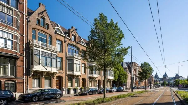 Straatbeeld van de Paulus Potterstraat in Amsterdam met karakteristieke herenhuizen, geparkeerde auto's en tramrails onder een blauwe lucht.