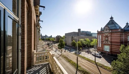 Zonnig uitzicht vanaf een balkon aan de Paulus Potterstraat in Amsterdam, met zicht op het straatbeeld en het karakteristieke gebouw van het Concertgebouw of nabijgelegen museum.