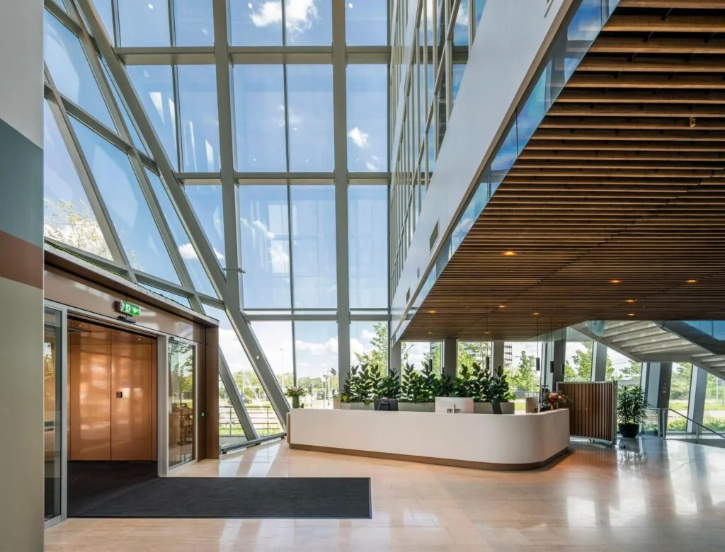 Moderne, lichte entreehal van een kantoorgebouw aan de David Ricardostraat met glazen gevel, houten plafond en een receptiebalie.