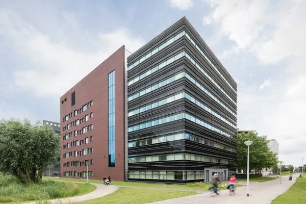 Een modern kantoorgebouw met een rode en zwarte gevel en een pad met fietsers op de voorgrond.