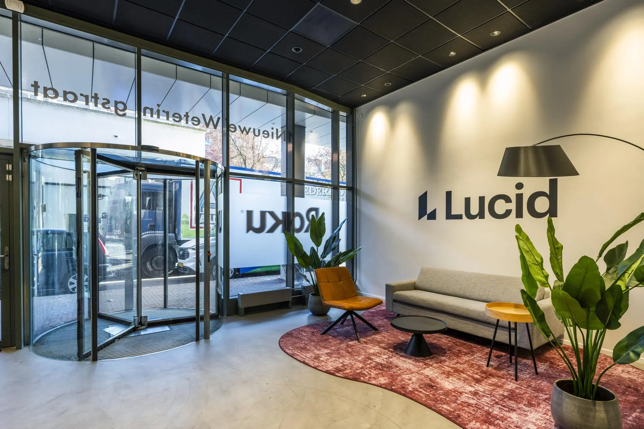 Moderne ontvangsthal van Lucid aan de Vijzelgracht met glazen draaideur, zitgedeelte en interieurplanten.