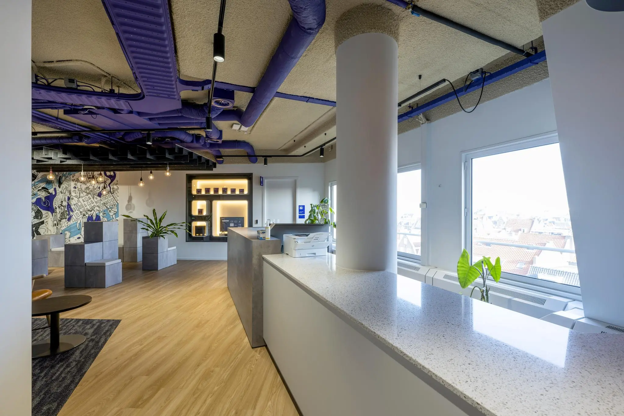 Modern kantoorinterieur aan de Vijzelgracht met een receptiebalie, open werkruimte, kunst aan de muur en paarse leidingen aan het plafond.