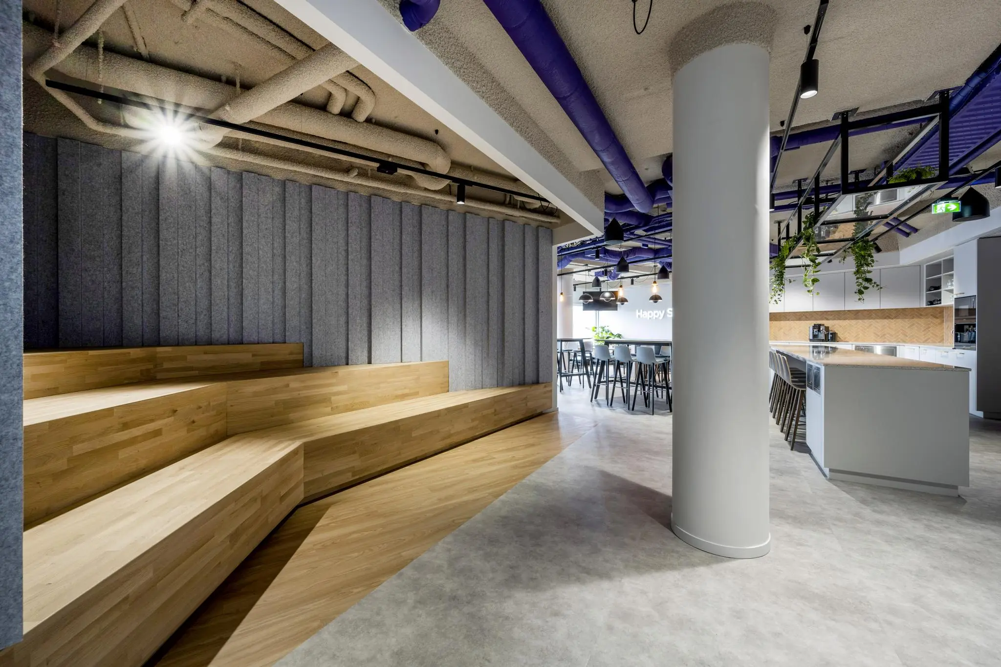 Modern kantoorinterieur aan de Vijzelgracht met houten tribunezitplaatsen, een open keuken en een zithoek met hoge tafels en krukken.