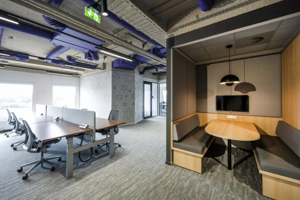 Modern kantoorinterieur aan de Vijzelgracht met flexwerkplekken en een vergaderruimte in nis met tv-scherm.