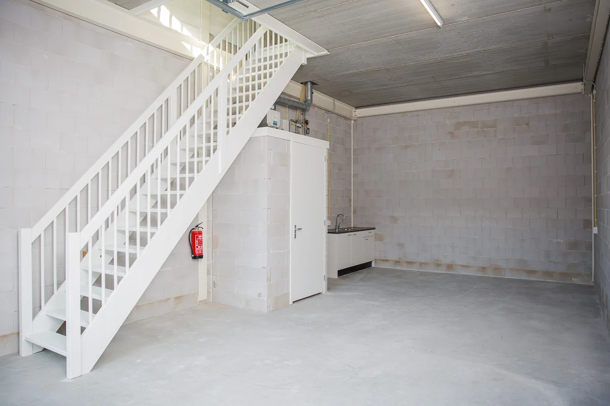 Lege bedrijfsruimte aan de Laan van 's-Gravenmade met betonnen vloer, witte trap, keukentje en techniekruimte.