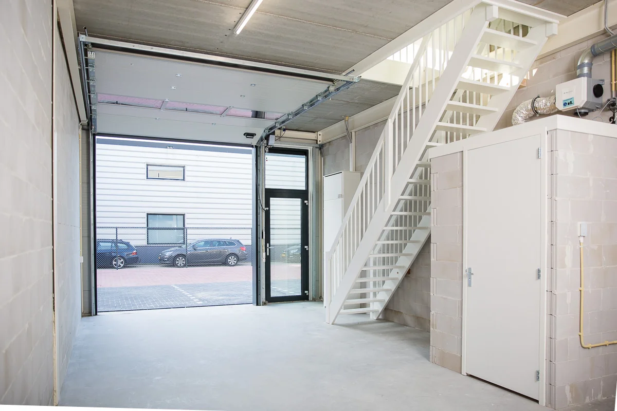 Interieur van een lichte bedrijfsunit aan de Laan van ’s-Gravenmade met open garagedeur, witte trap en afgesloten berging.