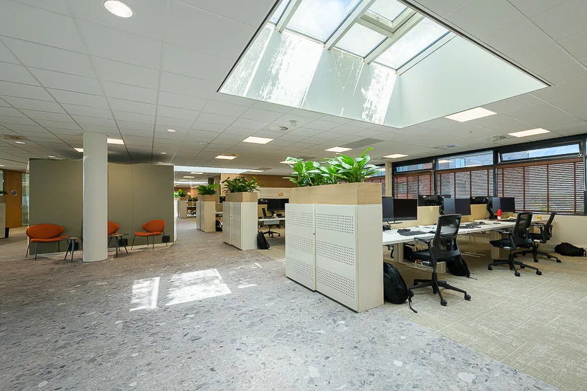 Modern open-plan office at Laan van Barcelona with skylight, workstations, and indoor greenery.