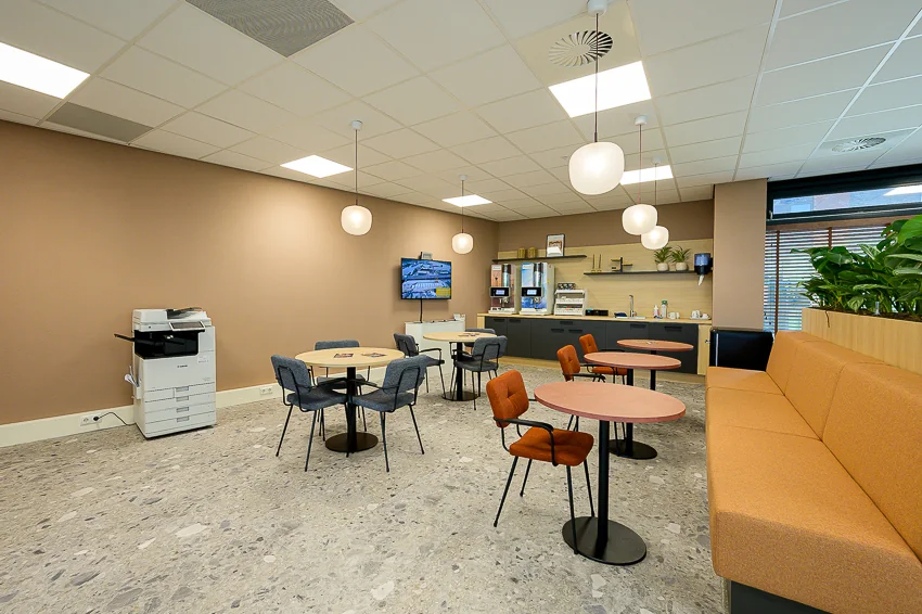 Modern office break room with round tables, a coffee corner, and a printer at Laan van Barcelona.