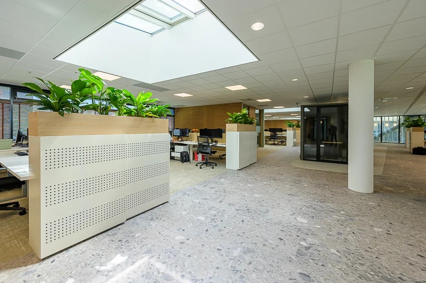Modern office interior on Laan van Barcelona with open workspaces, large planters, and natural light from a skylight.