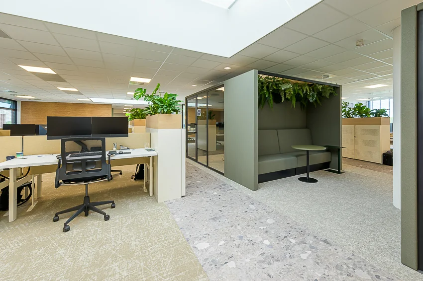 Modern open-plan office interior at Laan van Barcelona with workstations, a green meeting pod, and natural lighting.