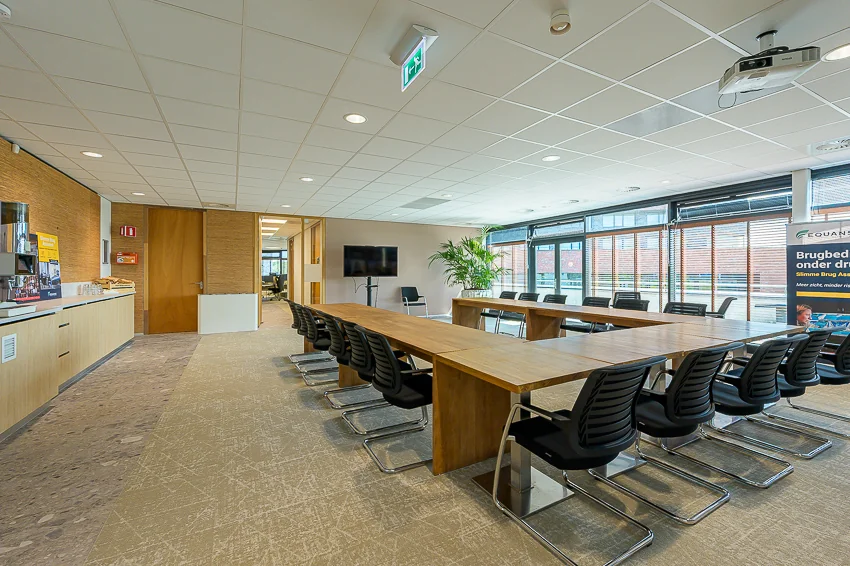 Modern conference room at Laan van Barcelona with a large wooden meeting table, black chairs, and presentation equipment.
