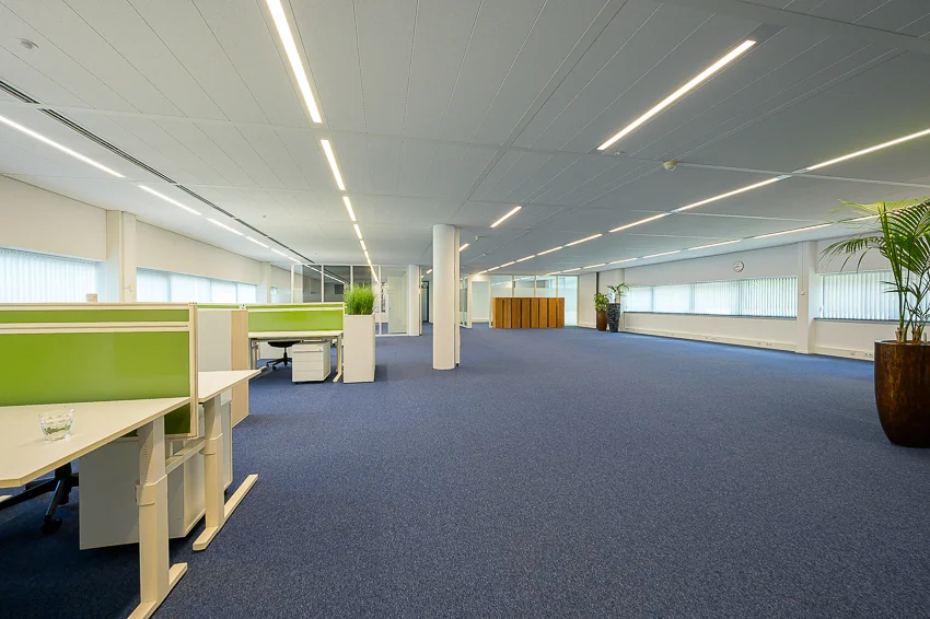 Spacious modern office interior at Laan van Barcelona with blue carpet, green desk dividers, and large windows.
