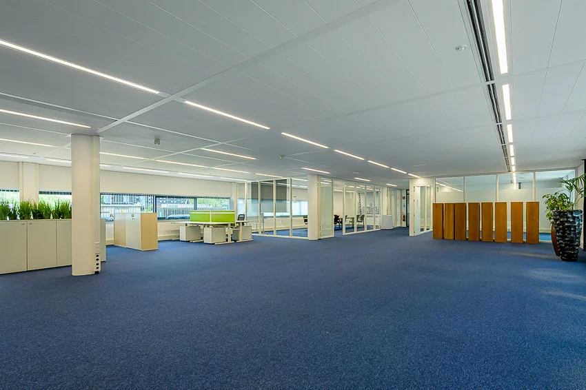 Modern open-plan office space with blue carpet, glass partitions, and minimalistic furniture at Laan van Barcelona.