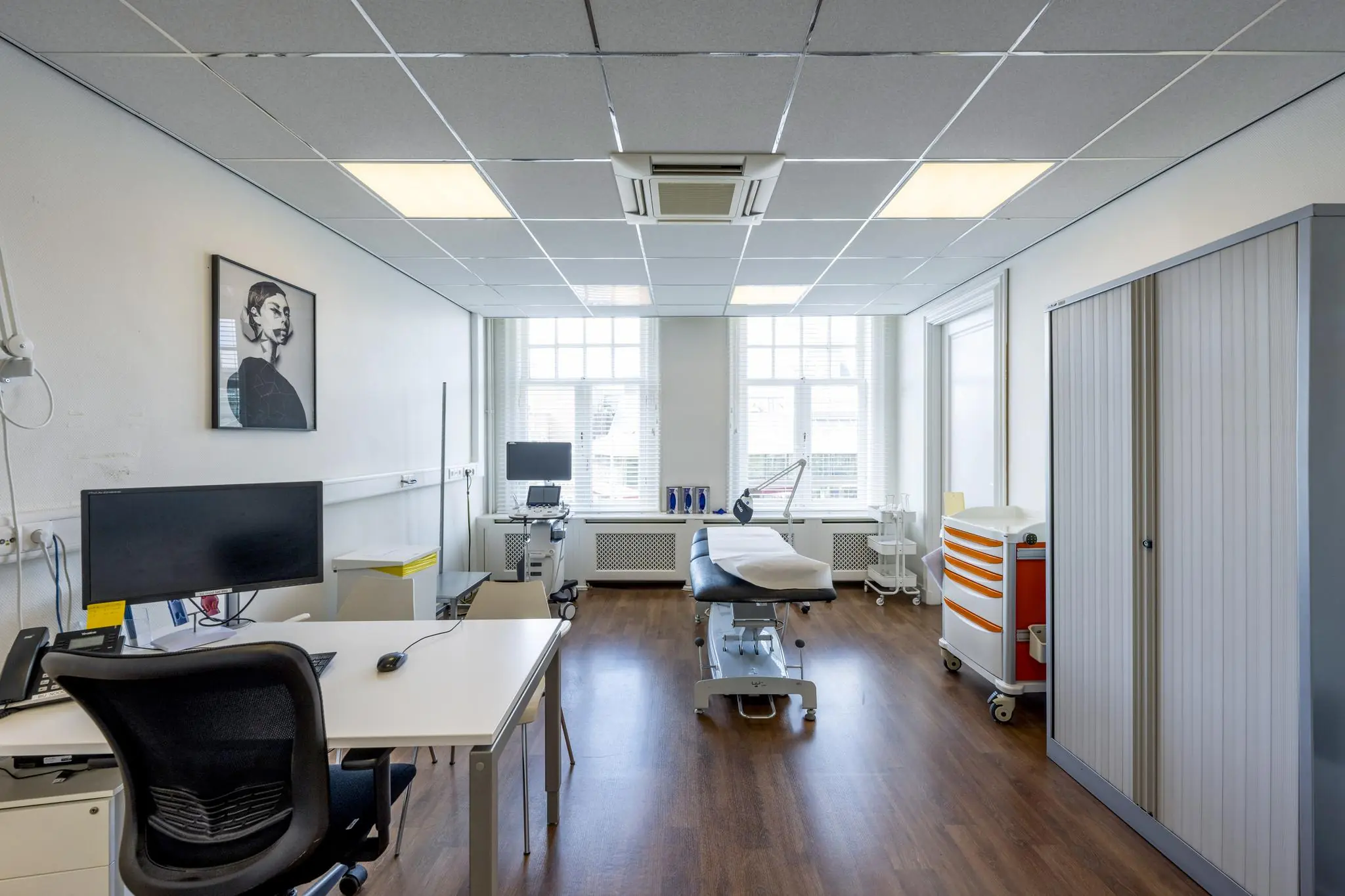 Lichte en moderne behandelkamer met bureaus, onderzoeksbank en medische apparatuur aan het Concertgebouwplein.
