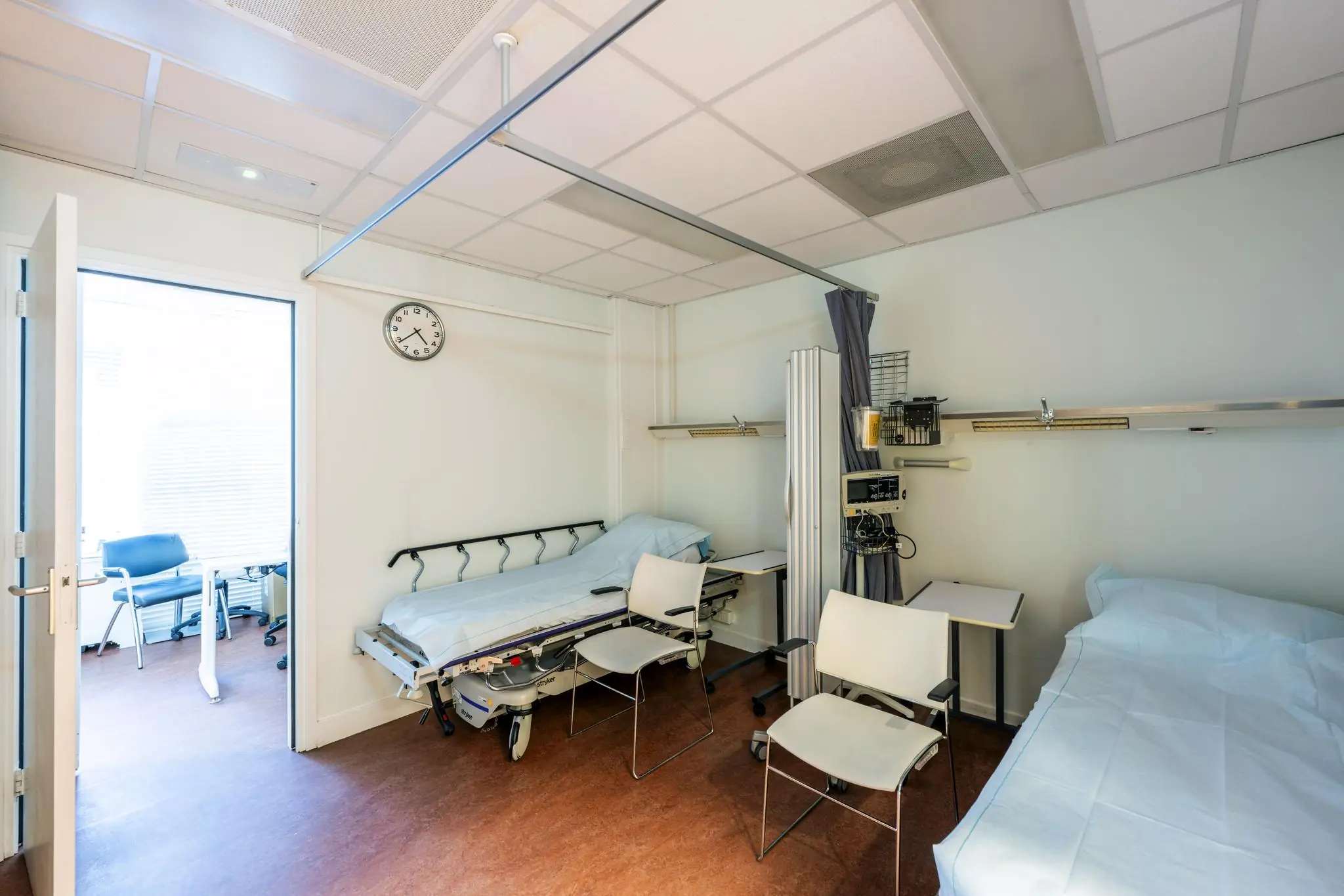 Een ziekenhuis- of behandelkamer met twee bedden, stoelen en medische apparatuur.