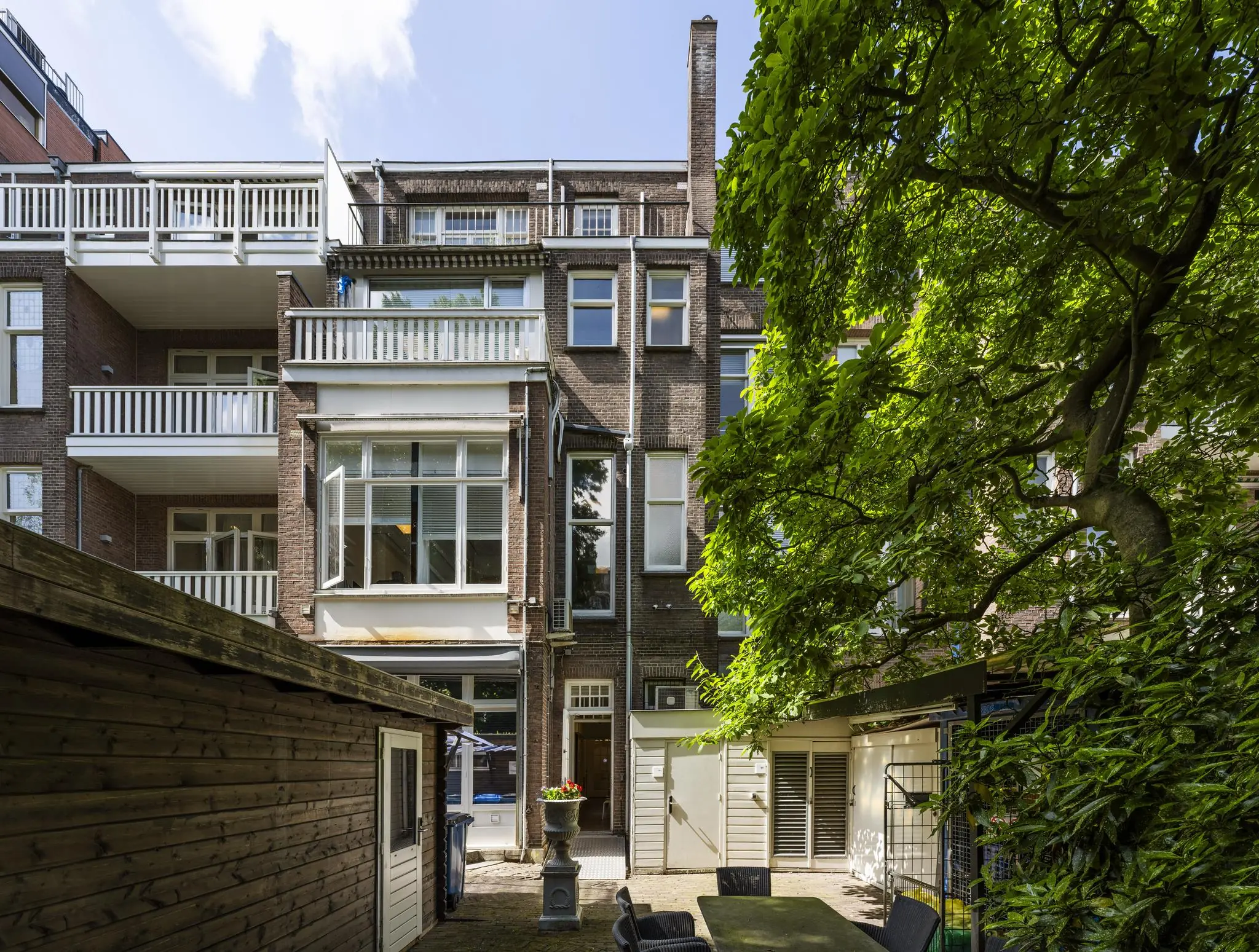 Achtergevel van een klassiek woongebouw aan het Concertgebouwplein met balkonnetjes, tuin en grote boom.