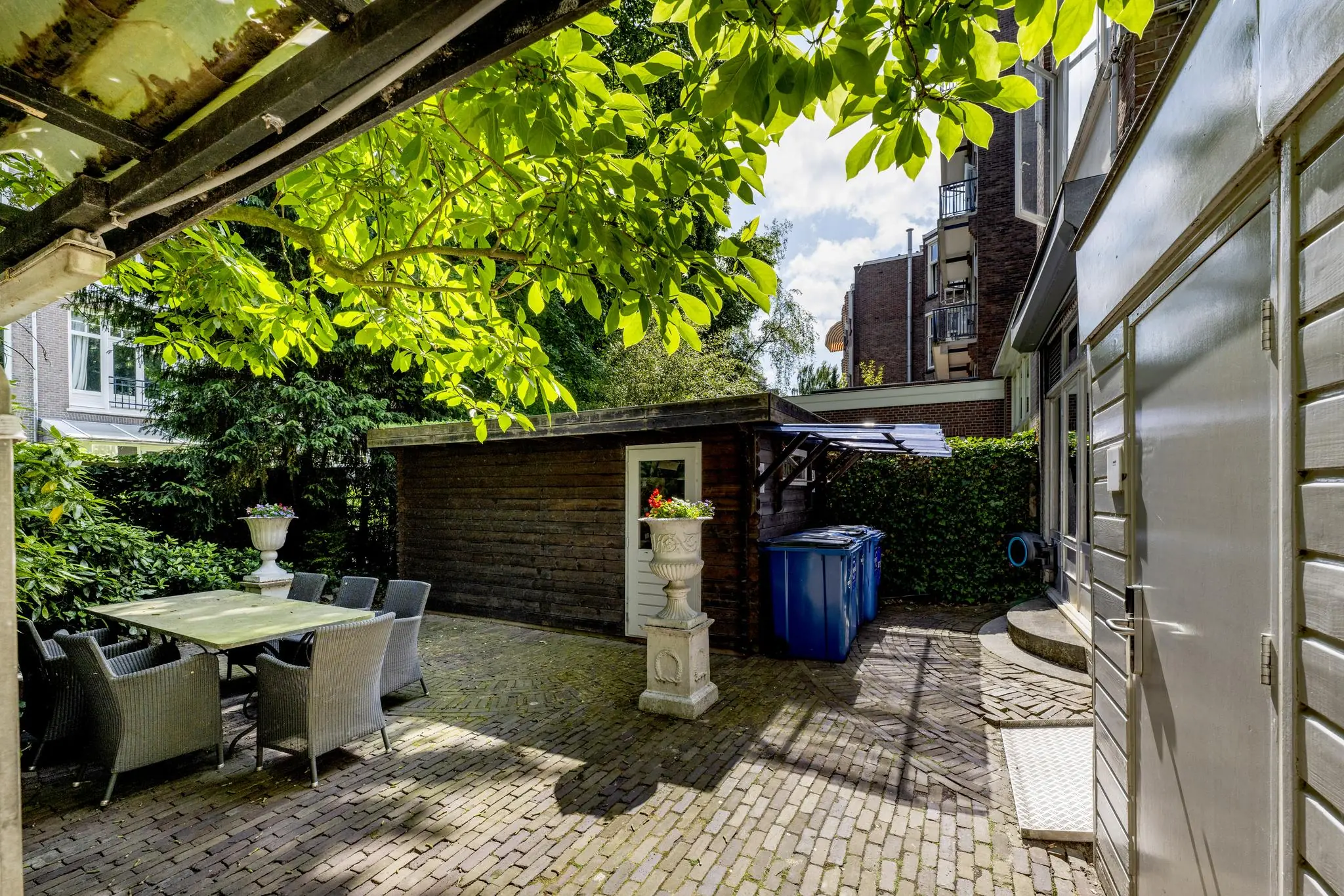 Binnentuin met tuinmeubilair, een houten schuurtje en bloeiende planten op het Concertgebouwplein.