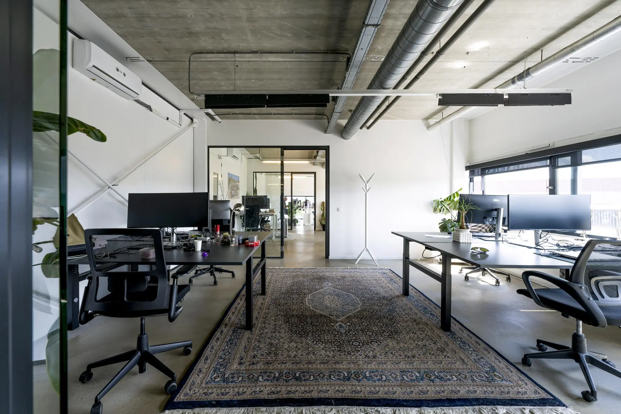 Modern kantoorinterieur aan de Johan van Hasseltweg met bureaus, computerschermen, een kleed en industriële plafondafwerking.