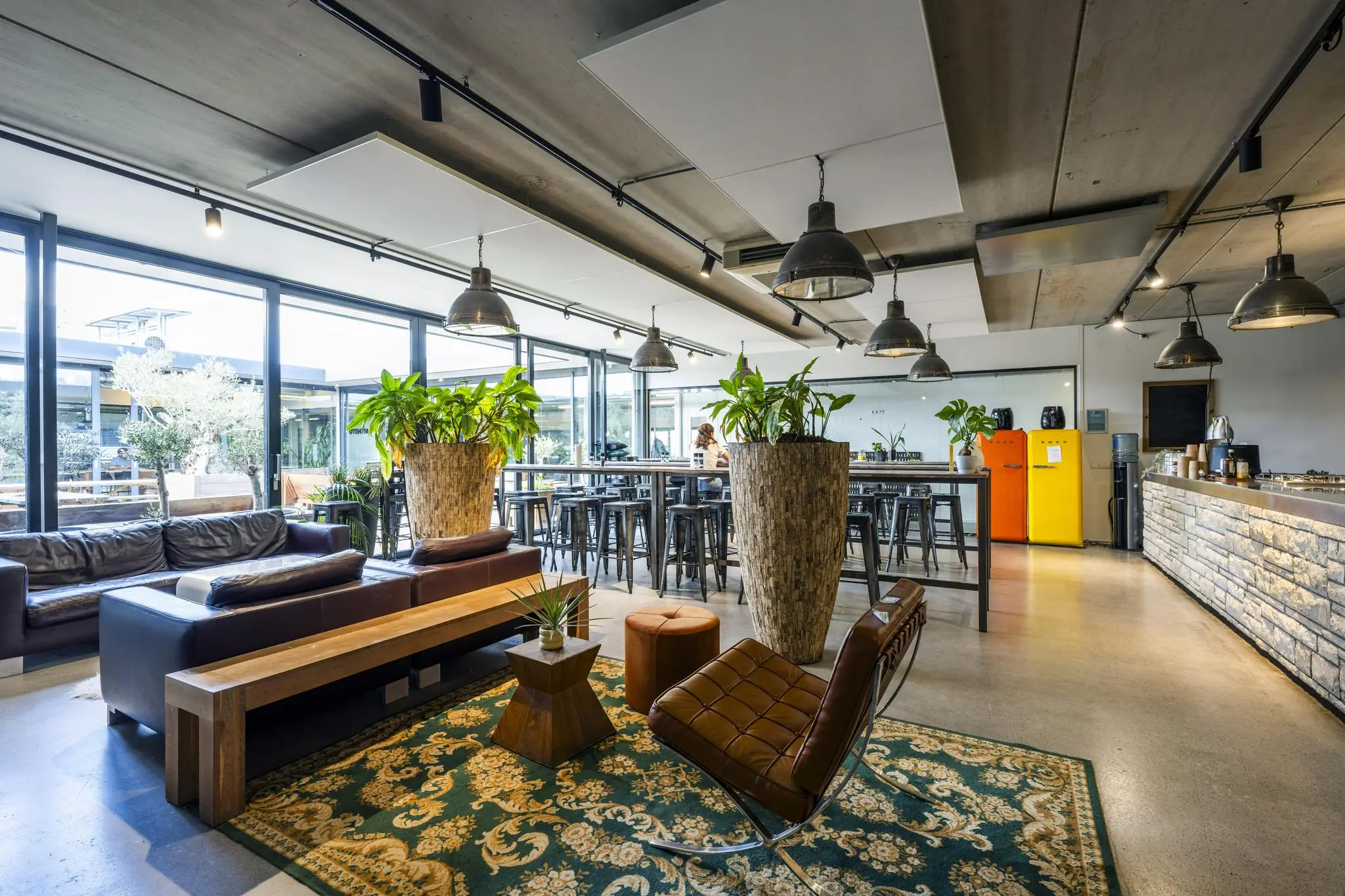 Modern ingerichte lounge- en eetruimte aan de Johan van Hasseltweg met veel daglicht, grote planten en kleurrijke retro koelkasten.