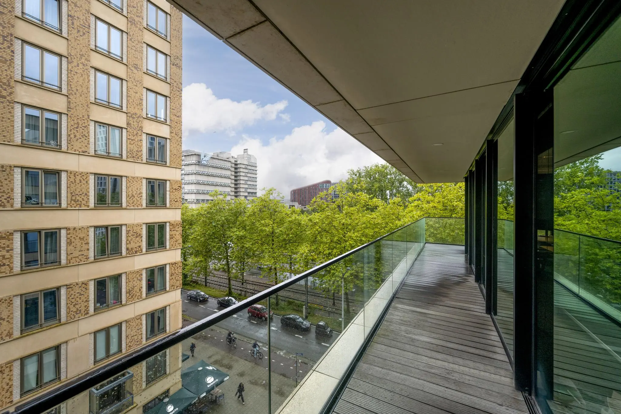 Zicht vanaf een modern balkon met glazen balustrade aan de Gustav Mahlerlaan, uitkijkend op stadspanden en een met bomen omzoomde straat.