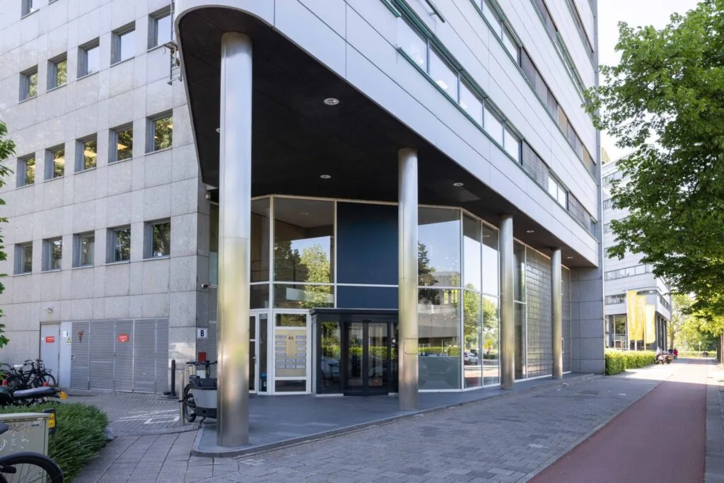 Ingang van een modern kantoorpand aan de Overschiestraat in Amsterdam met glazen gevel en stalen zuilen.