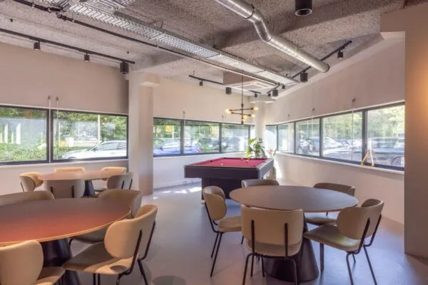 Moderne kantineruimte aan de Overschiestraat met ronde tafels, designstoelen en een pooltafel bij grote ramen.
