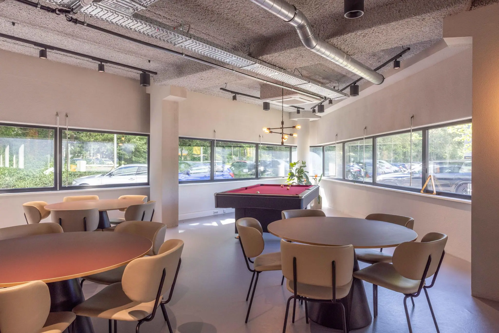 Moderne kantineruimte aan de Overschiestraat met ronde tafels, designstoelen en een pooltafel bij grote ramen.