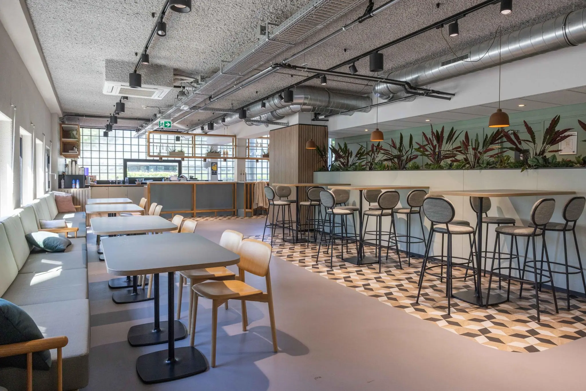 Moderne en lichte kantineruimte aan de Overschiestraat met zitgedeelte, hoge tafels en industriële plafondafwerking.