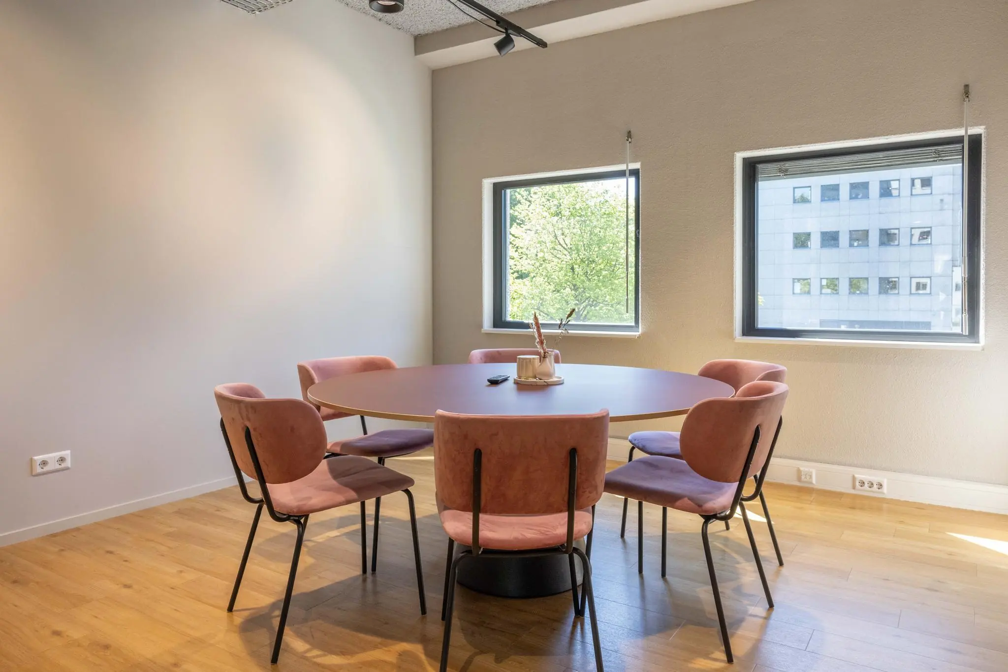 Vergaderruimte aan de Overschiestraat met ronde tafel, zes roze stoelen en uitzicht op een kantoorpand.