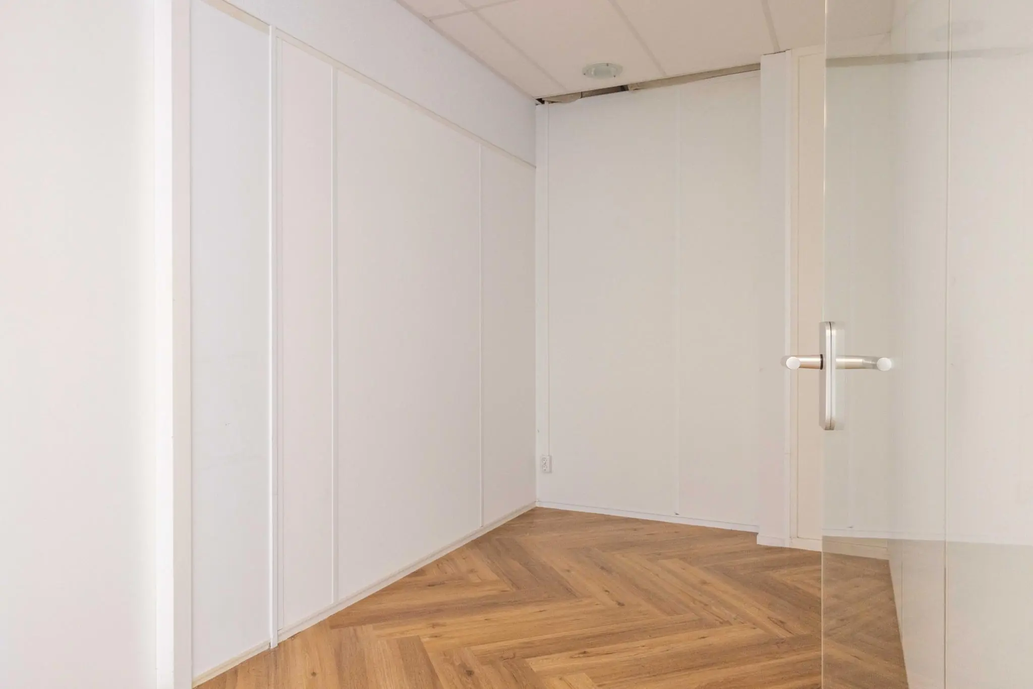 Kleine, lege kamer met witte wanden, visgraat houten vloer en een glazen deur in de Overschiestraat.