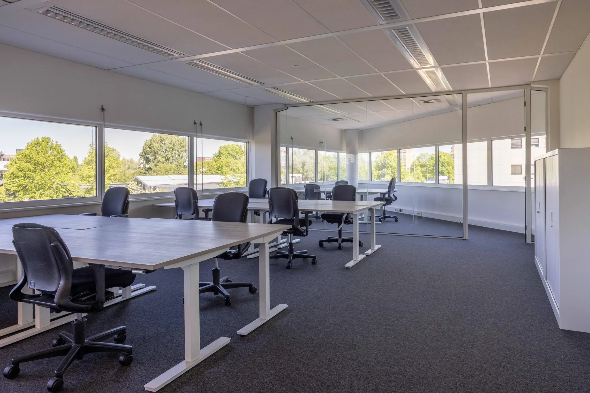 Modern kantoorinterieur aan de Overschiestraat met meerdere bureaus, bureaustoelen en grote ramen met uitzicht op groen.