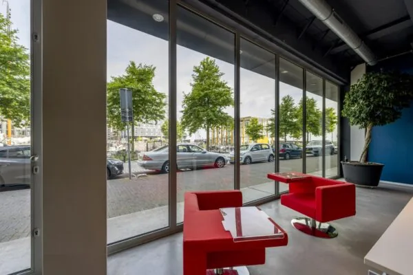 Zithoek met rode stoelen en glazen tafel bij hoge ramen met uitzicht op de Krijn Taconiskade in Amsterdam.