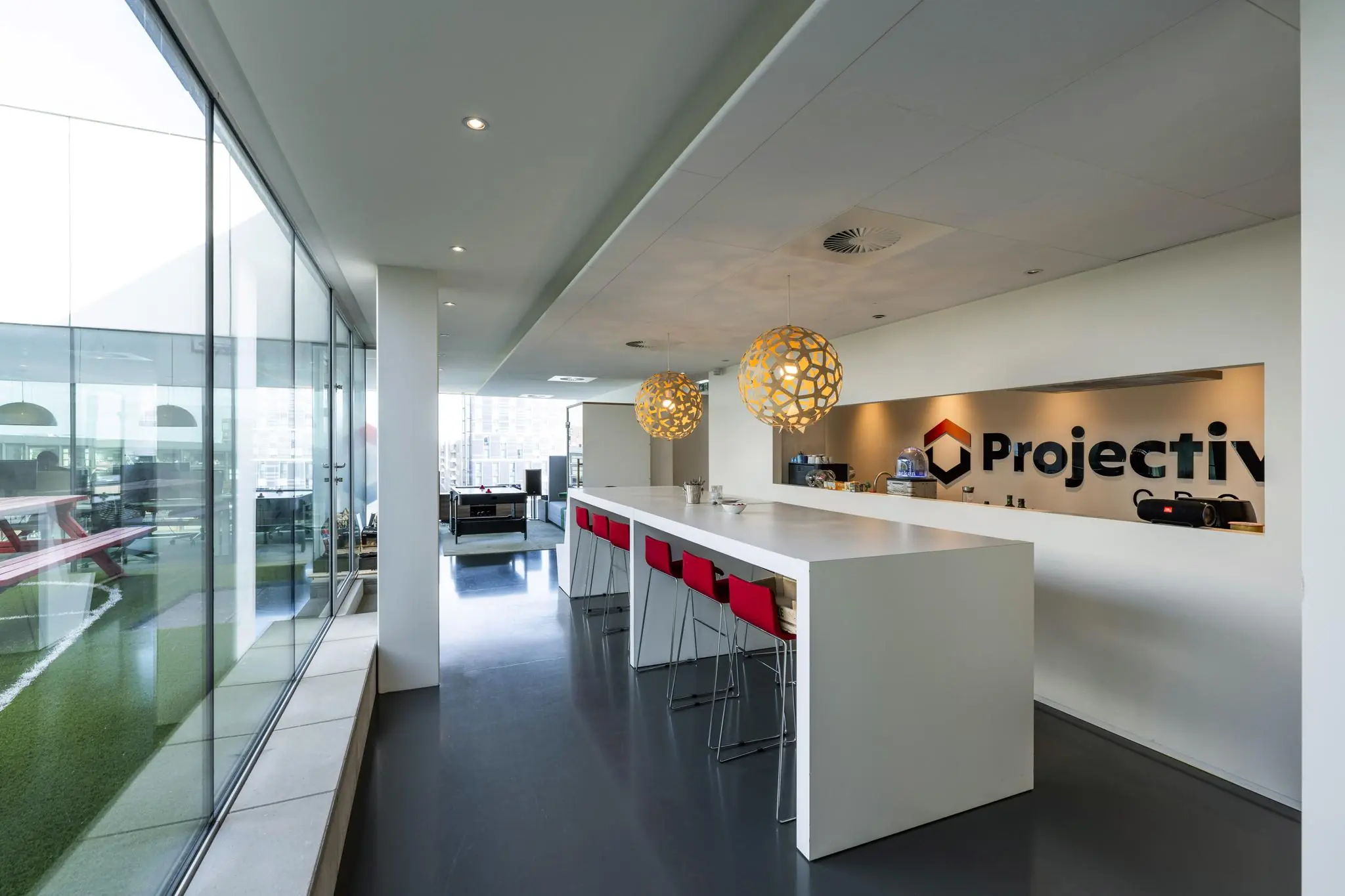 Moderne kantoorruimte aan de Krijn Taconiskade met een strakke bar, rode barkrukken, en het logo van Projectiv op de muur.