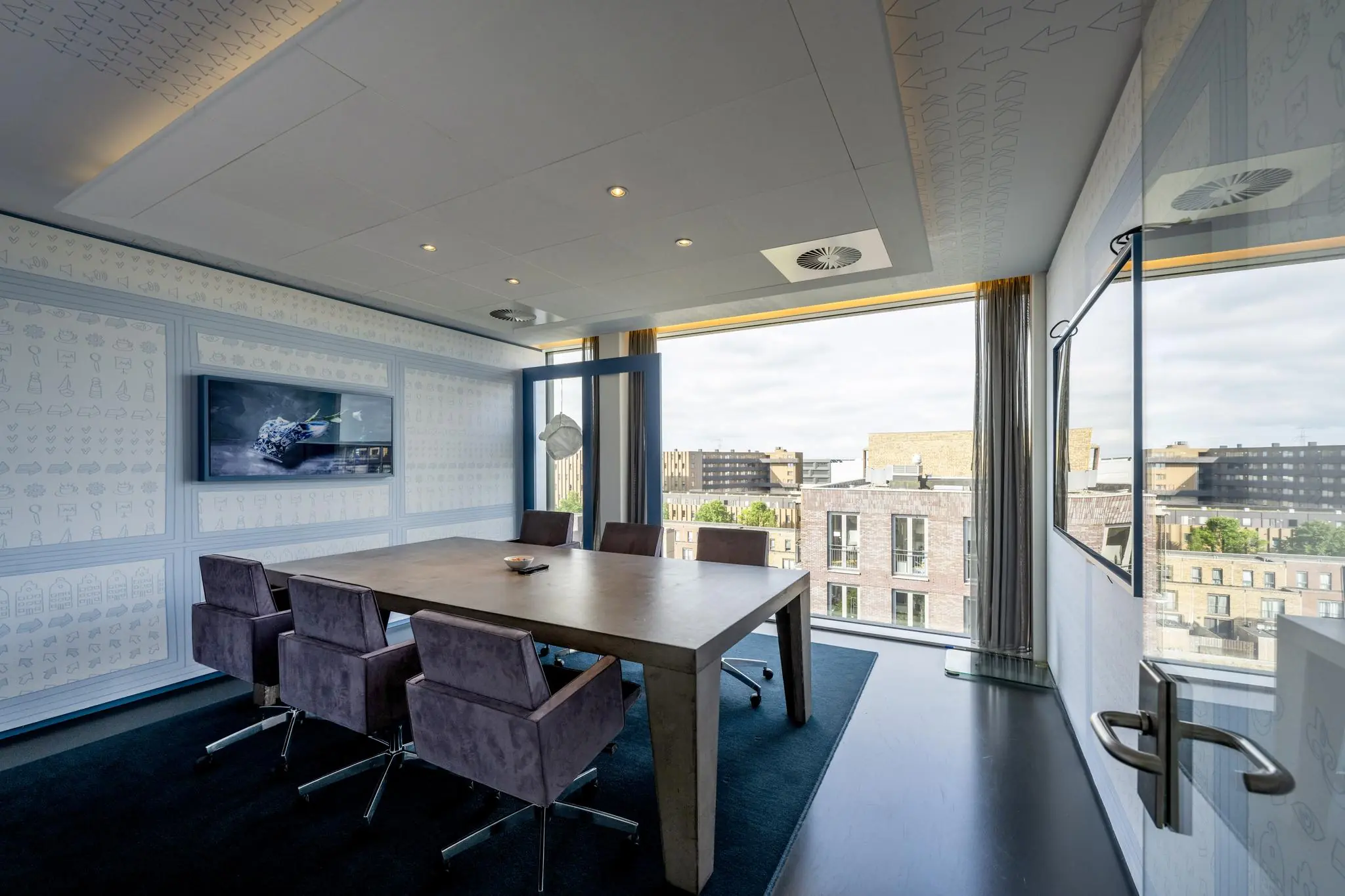 Vergaderruimte met zes stoelen, een houten tafel, een flatscreen en uitzicht op de Krijn Taconiskade in Amsterdam.