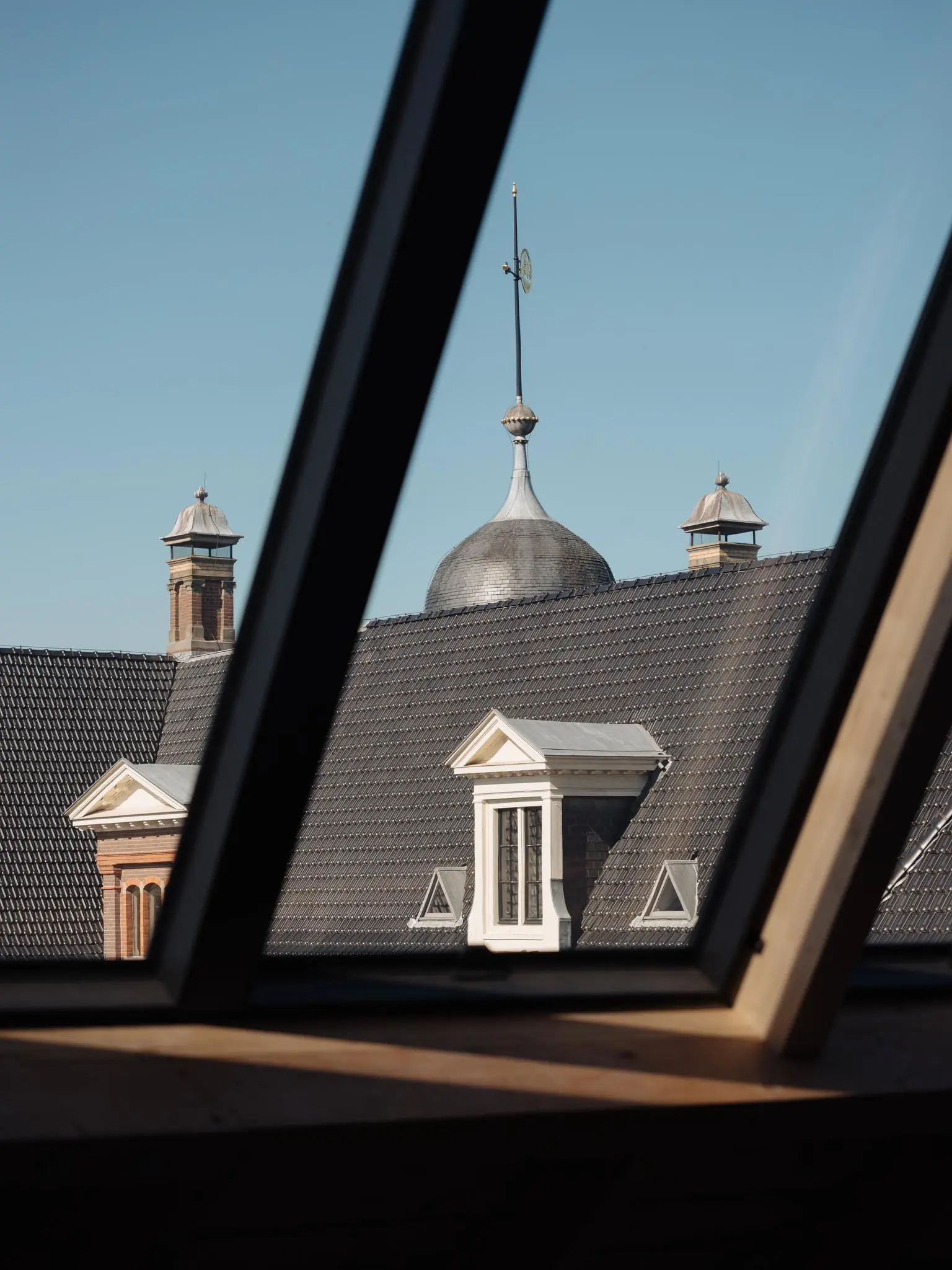 Uitzicht door een dakraam op het karakteristieke dak en de toren van een historisch gebouw aan de Leidseweg.
