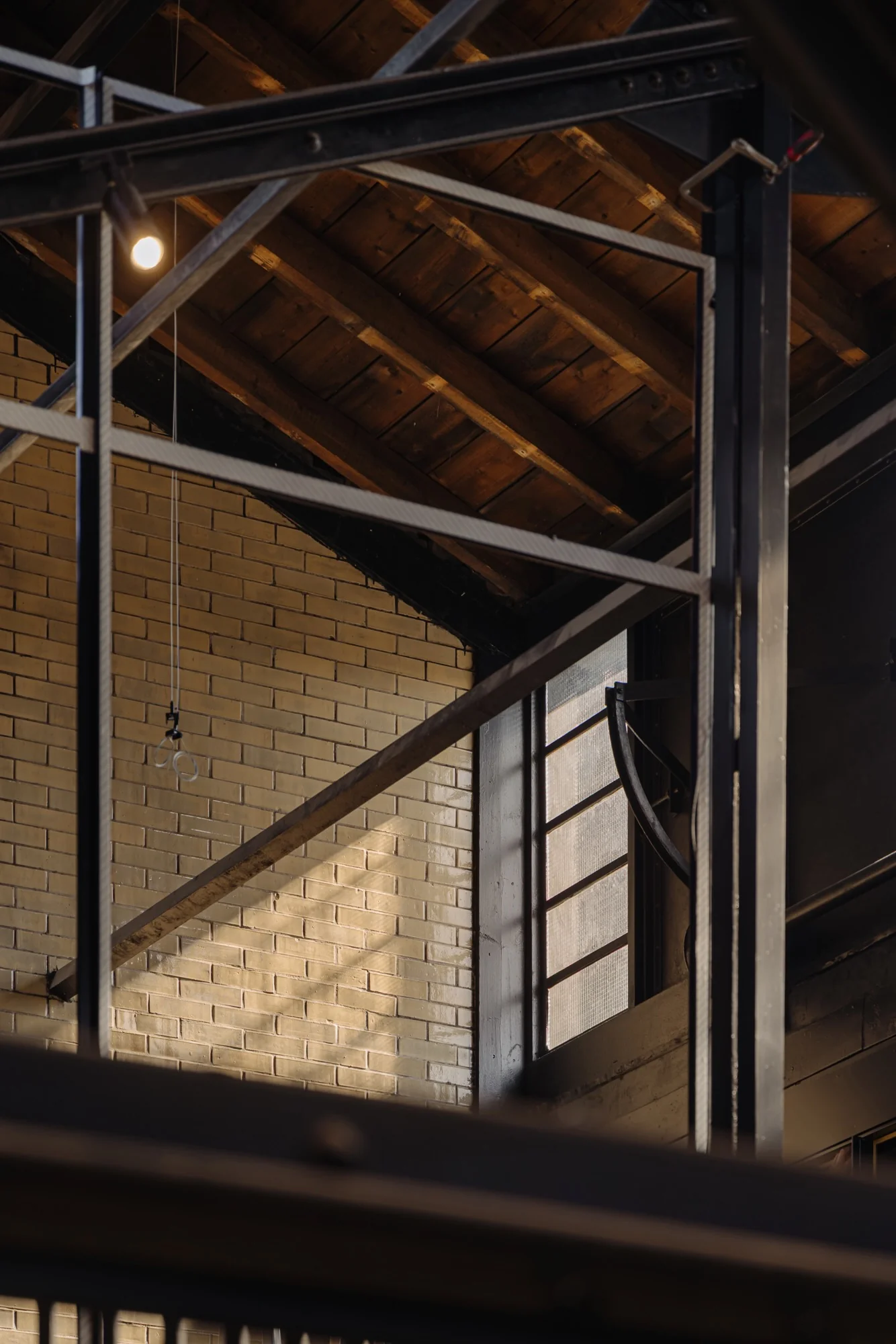 Detail van een industrieel interieur aan de Leidseweg met zicht op een bakstenen muur, houten dakconstructie en metalen raamkozijn.