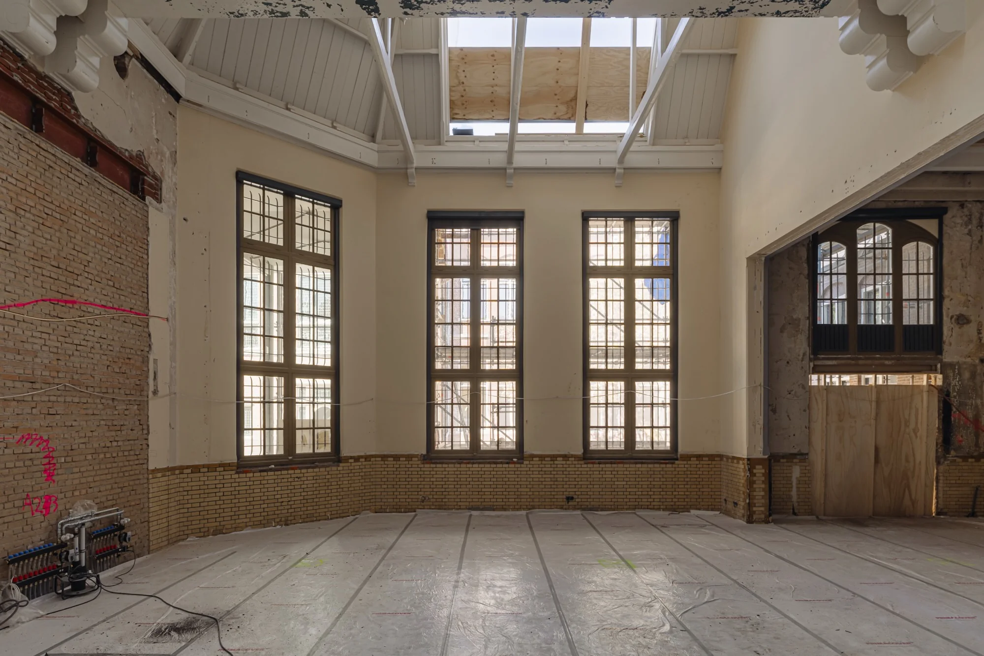 Een grote, hoge ruimte aan de Leidseweg in renovatie met hoge ramen, bakstenen muren en een gedeeltelijk open plafond.
