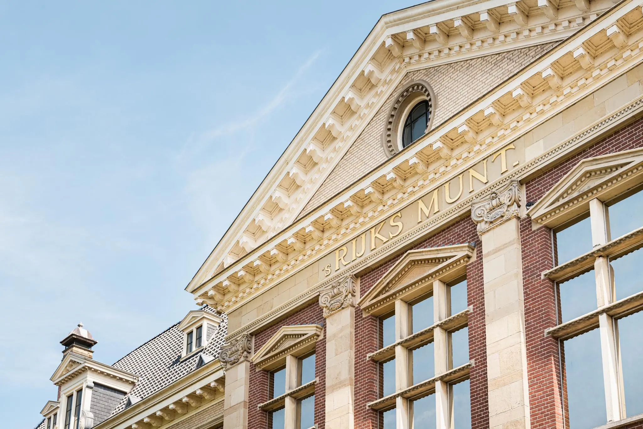 Voorgevel van het historische gebouw 's Rijks Munt met klassieke architectuur en rijk gedecoreerde elementen.