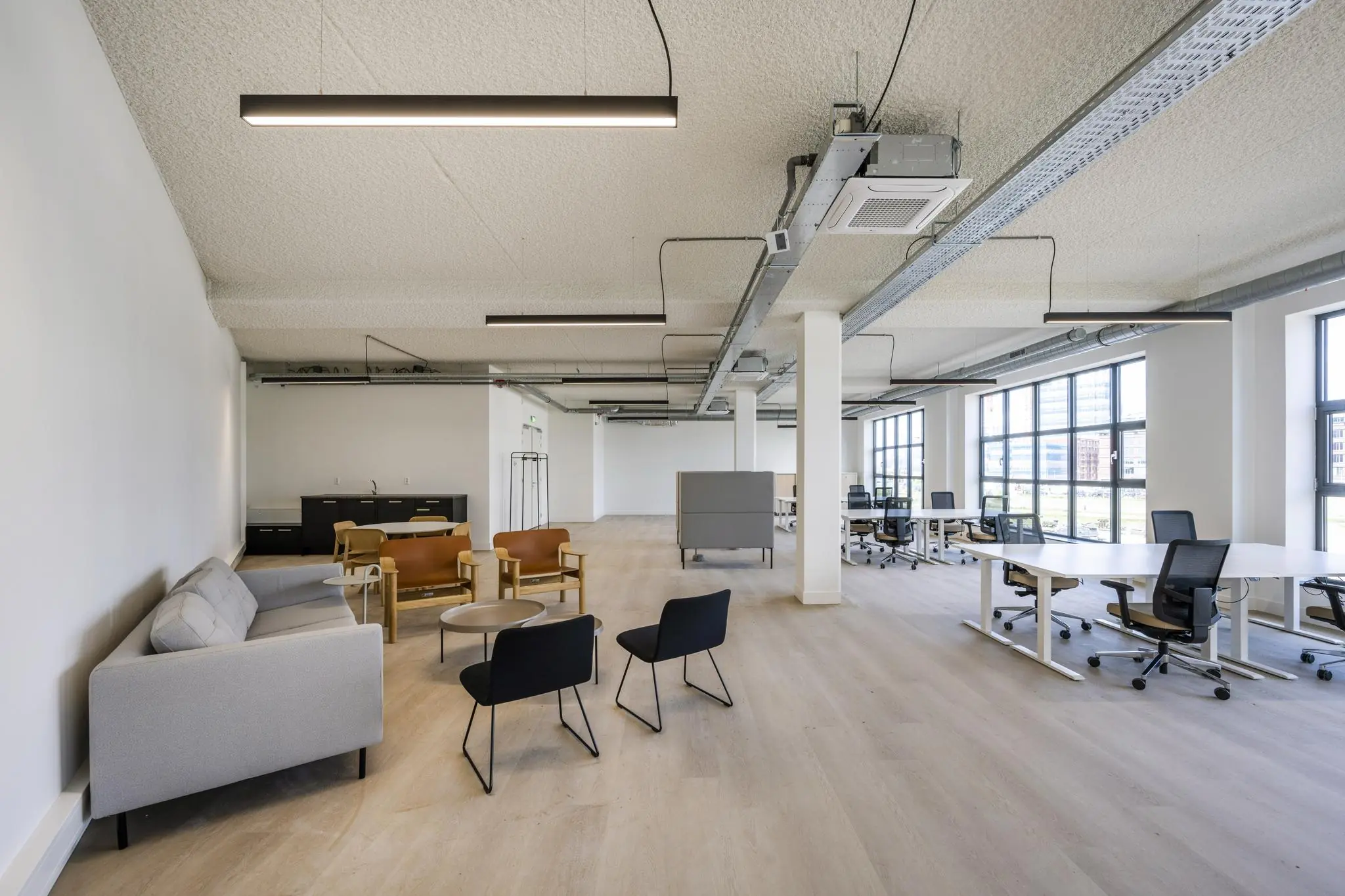 Moderne, lichte kantoorruimte met open werkplekken en een zithoek met stoelen en banken.