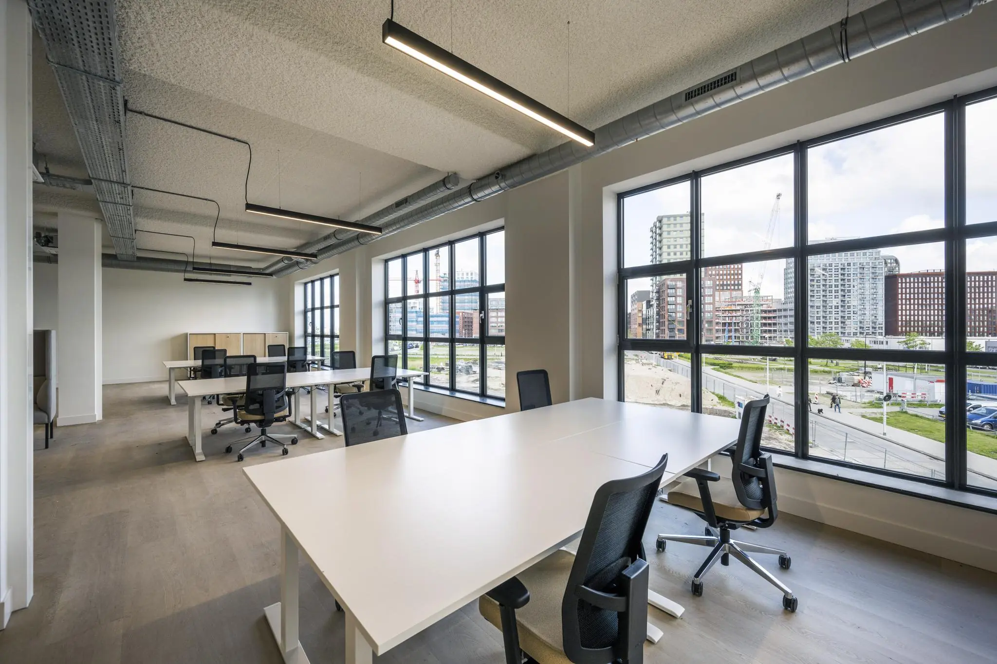 Moderne, lichte kantoorruimte met meerdere bureaus en grote ramen met uitzicht op nieuwbouw rondom de Hellingbaan.