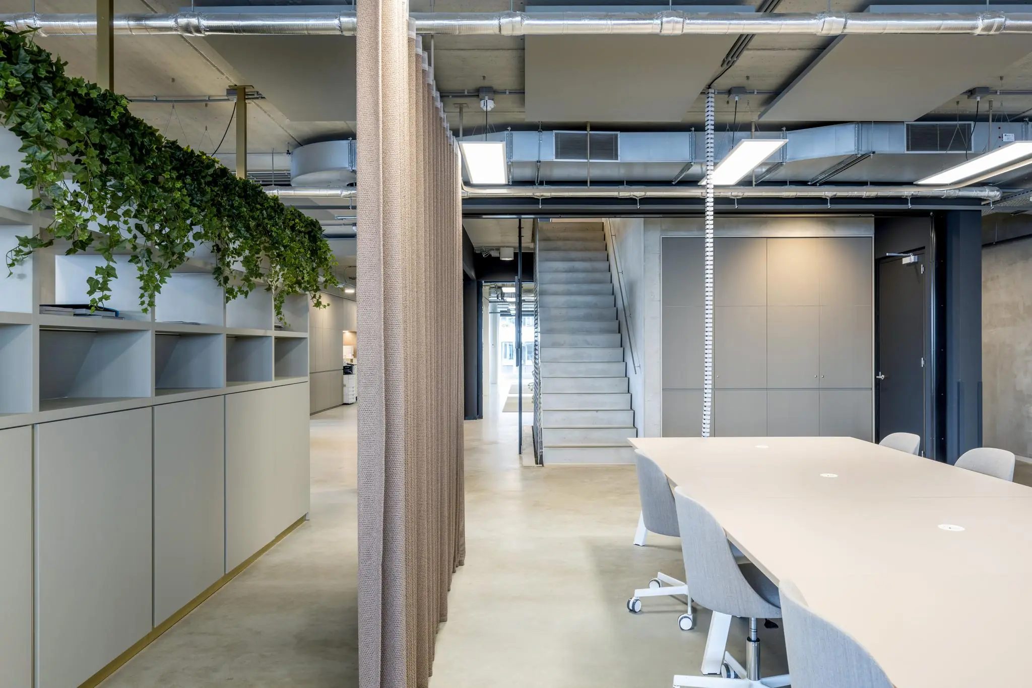 Moderne kantoorruimte aan de Moermanskade met vergadertafel, open trap en groene hangplanten boven opkasten.