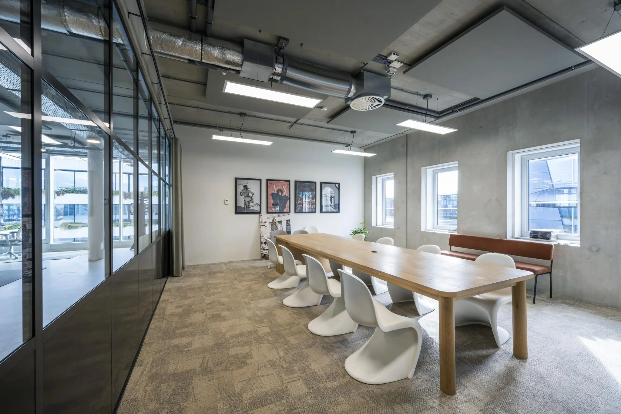 Vergaderruimte aan de Moermanskkade met een lange houten tafel, moderne witte stoelen, industriële plafonddetails en kunst aan de muur.