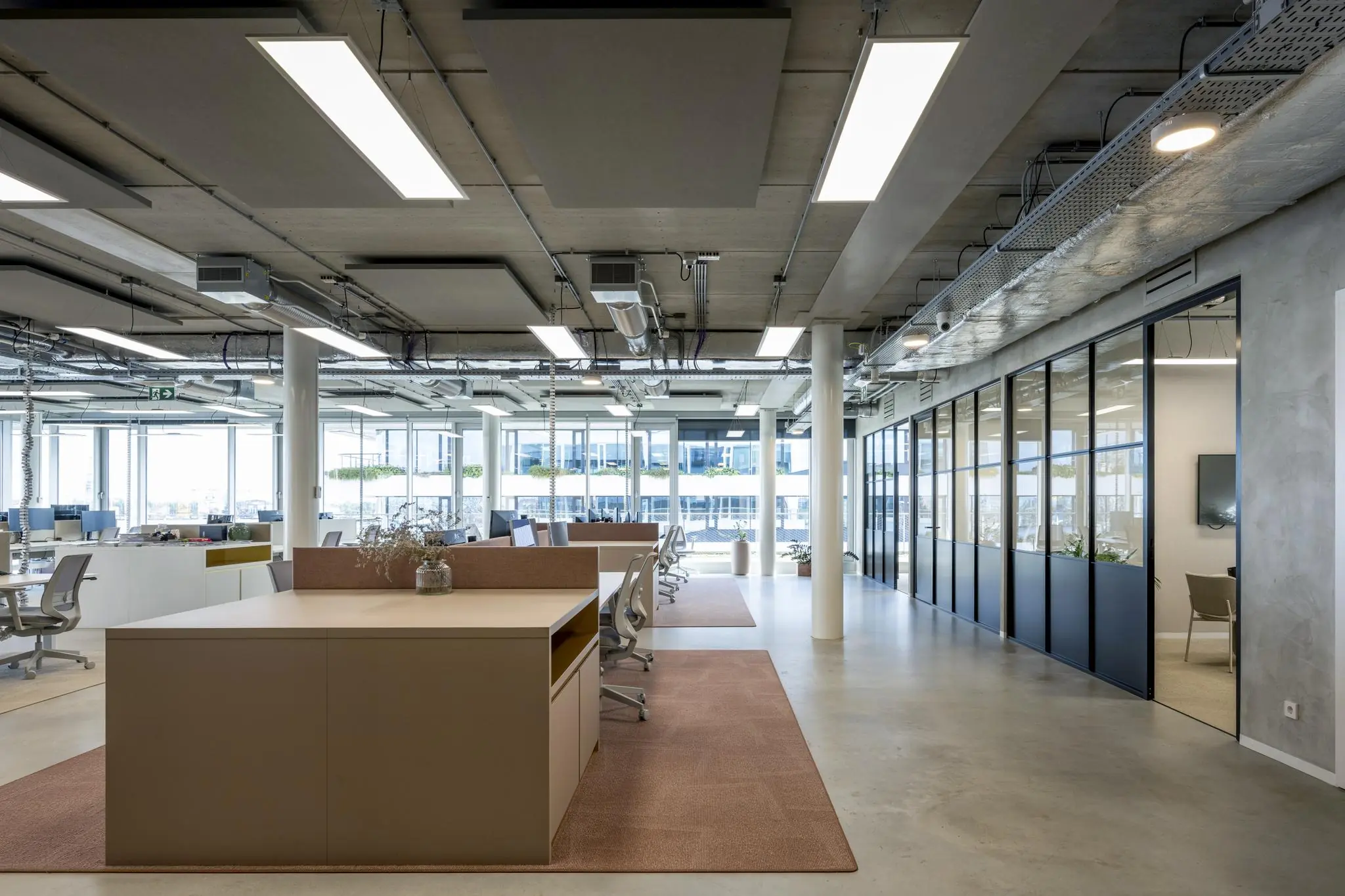 Modern kantoorinterieur aan de Moermanskade met open werkplekken, glazen vergaderruimtes en industriële plafondafwerking.