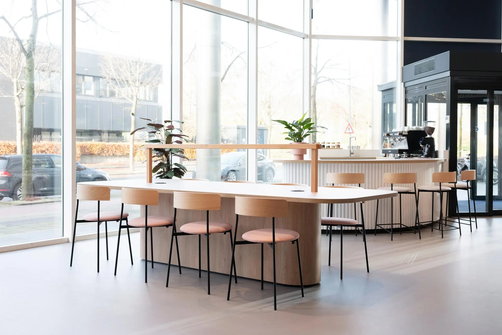 Moderne en lichte koffiebar met grote ramen, houten meubels en planten aan de Overschiestraat.