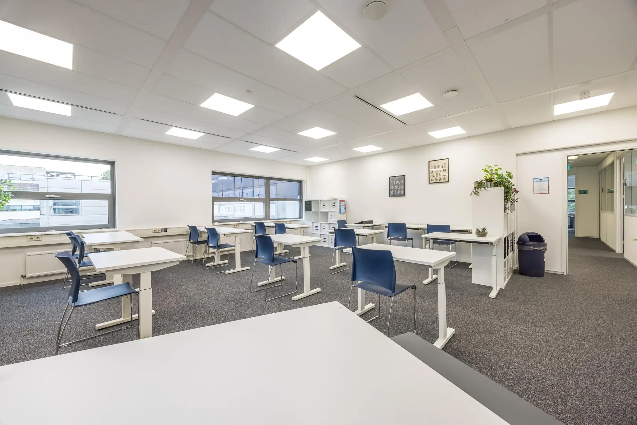 Licht en modern klaslokaal aan de Daltonlaan met losse bureaus, blauwe stoelen en grote ramen.
