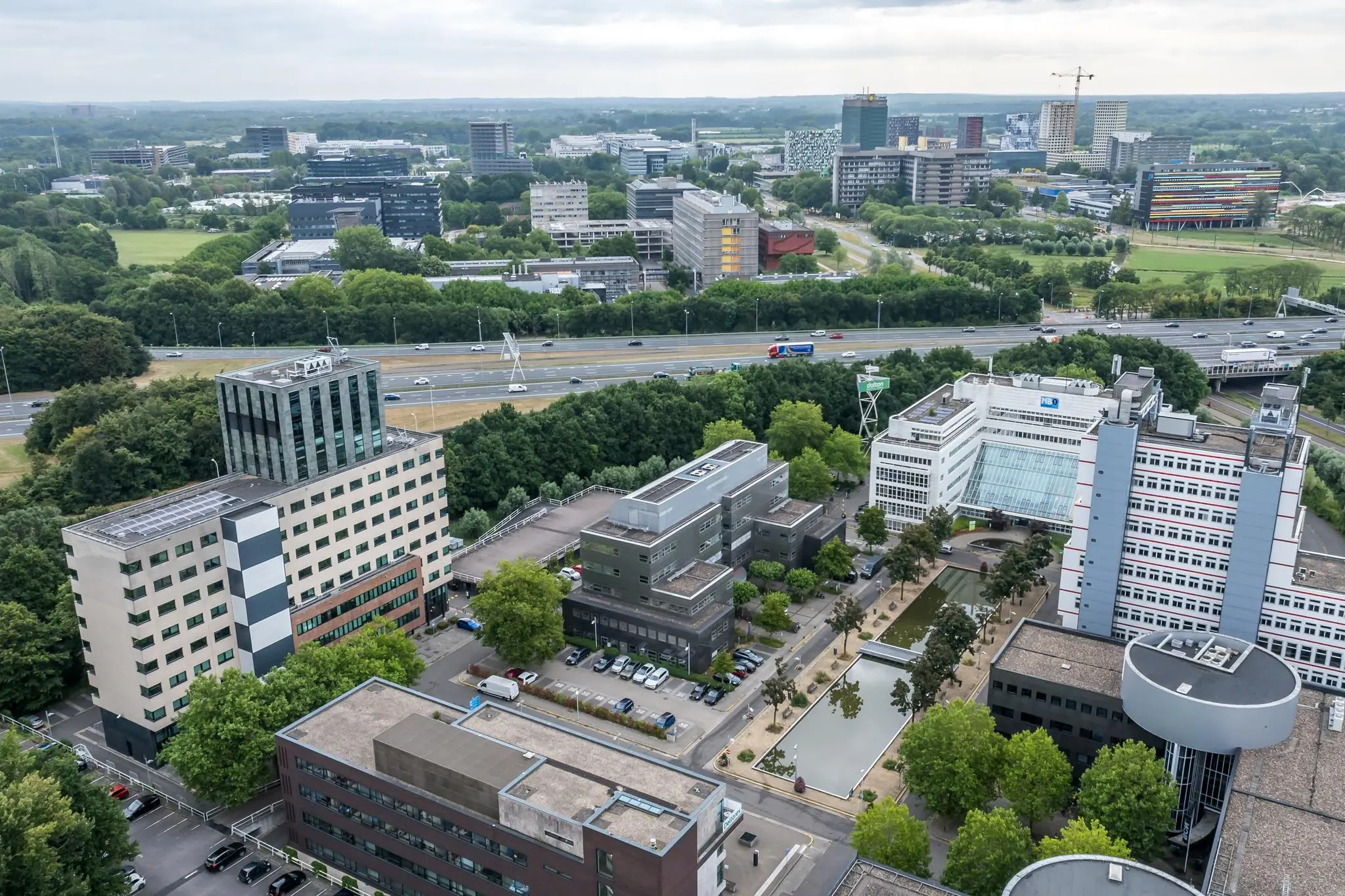 Luchtfoto van het kantoorgebied aan de Daltonlaan in Utrecht met diverse moderne gebouwen, vijvers en een snelweg op de achtergrond.
