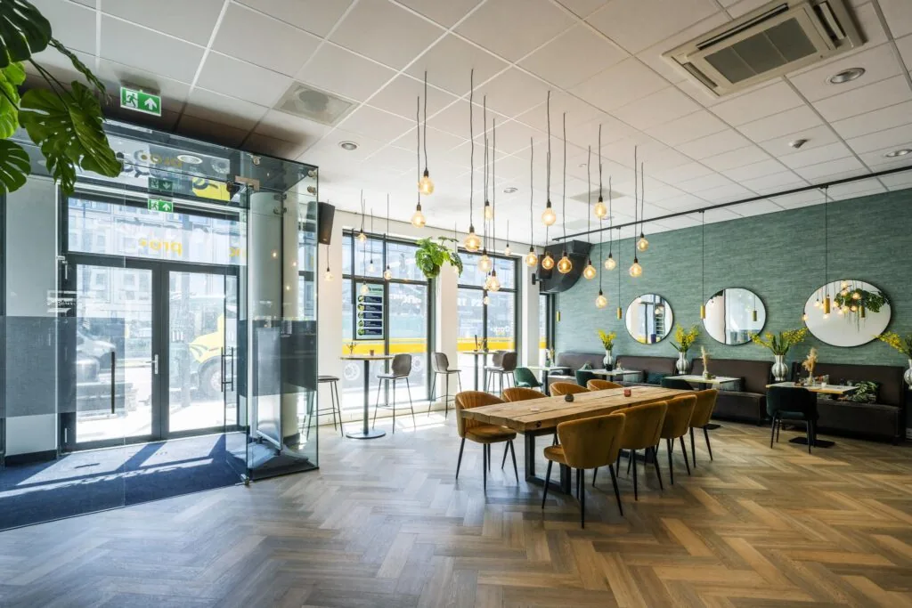 Modern en licht restaurantinterieur aan het Elizabeth Cady Stantonplein met houten vloer, lange eettafel en sfeerverlichting.