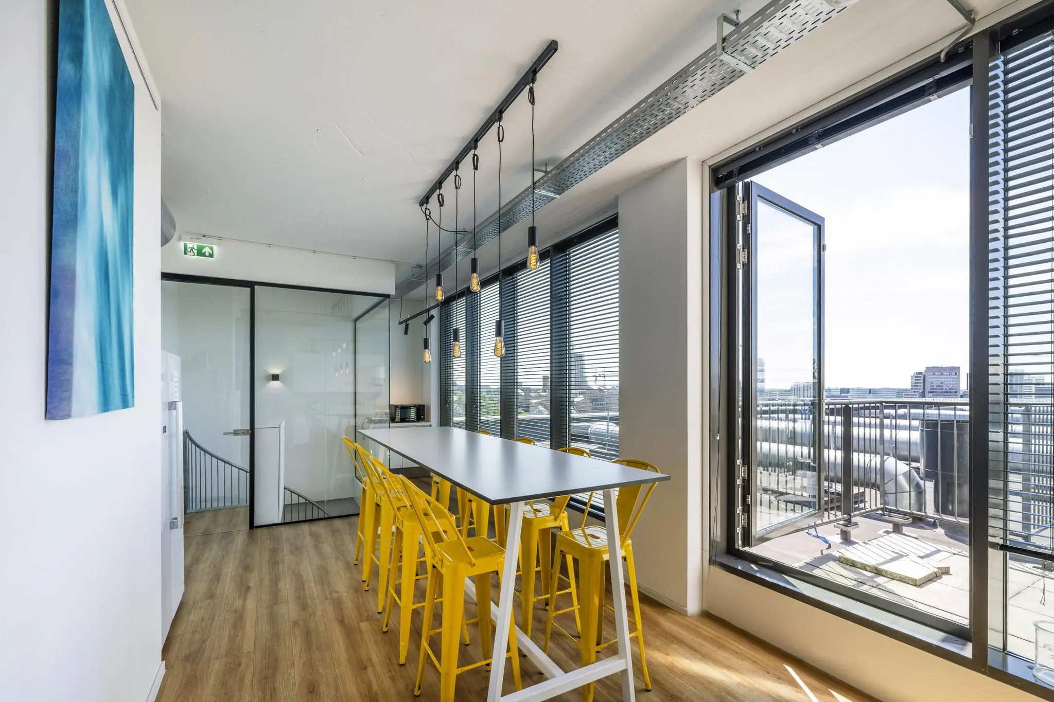 Moderne vergaderruimte met lange tafel, gele barkrukken en uitzicht op het Elizabeth Cady Stantonplein via een open glazen deur.